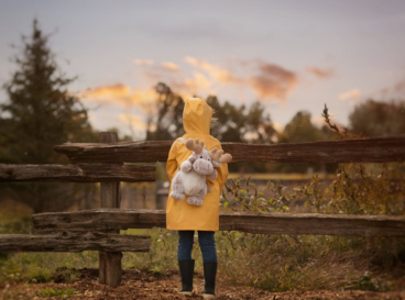Enfant en ciré jaune vu de dos tenant une peluche, regardant l’horizon au coucher du soleil